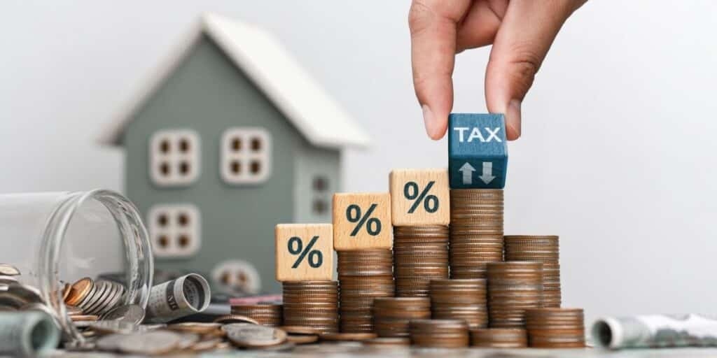 Coins stacked with percentage blocks and tax cube near a model house illustrating capital gains tax on inherited property when selling a home