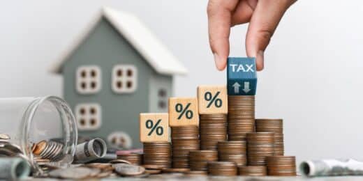 Coins stacked with percentage blocks and tax cube near a model house illustrating capital gains tax on inherited property when selling a home